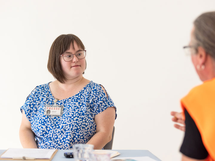 Eine Jungs Frau mit blaugemusterten Top ist im Gespräch mit einem Mann in Leuchtweste