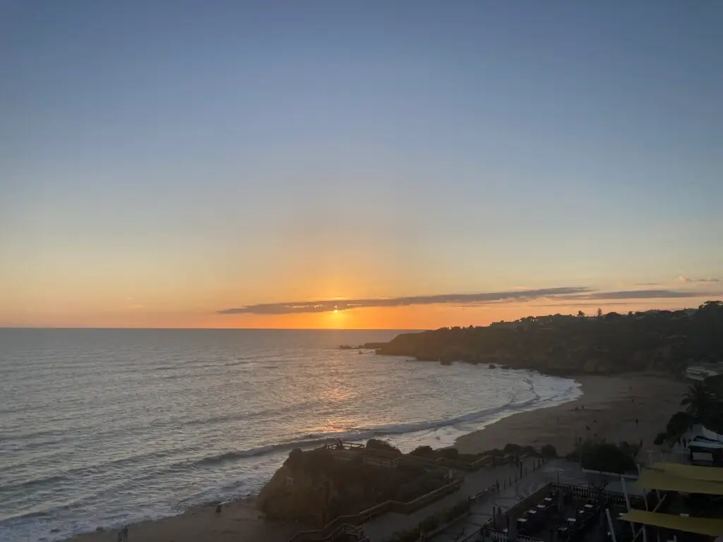 Blick auf die Algarve Küste. Sonnenuntergang, links das Meer, rechts die Küste, blauer und wolkenloser Himmel.