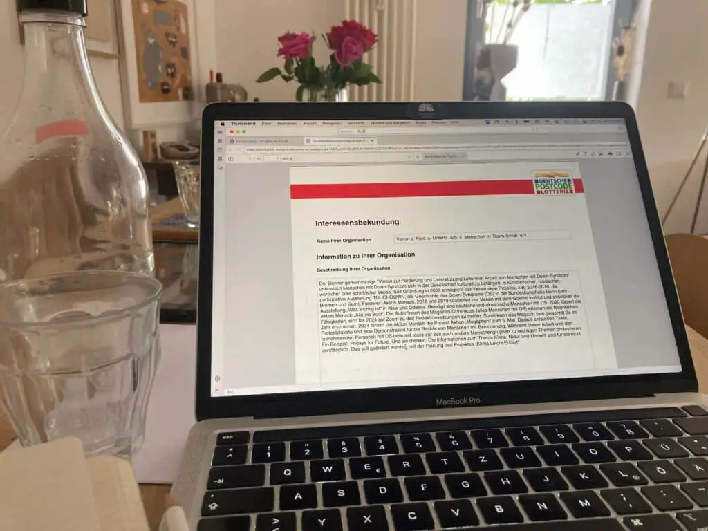 Ein aufgeklappter Laptop. Auf dem Bildschirm siehst Du ein Formular. Links daneben steht ein Wasserglas und eine Flasche.
