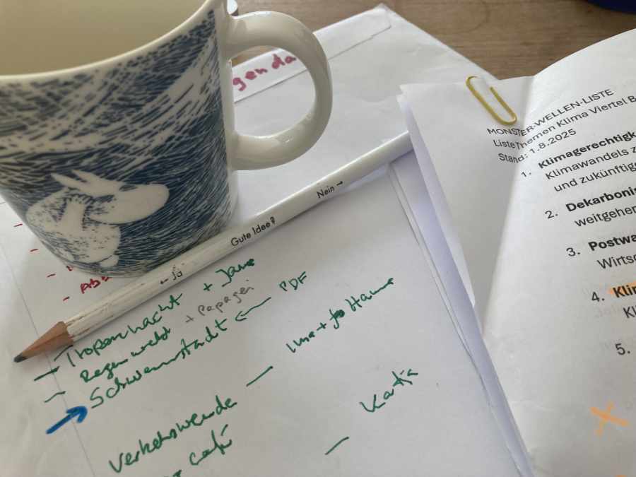 Blick von oben auf eine Tasse, mit Mumin Motiv. Die Tasse steht auf einem Zettel, mit Notizen. Rechts sieht man die Ecke eines ausdruckten Blattes, mit einer Liste. Vor der Tasse liegt ein Bleistift.