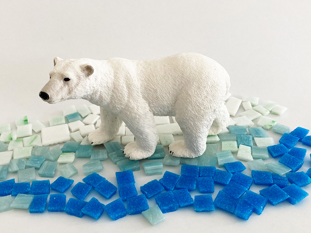 Auf dem Foto sieht man eine Miniatur von einem Eisbären. Er steht auf blauen und weißen Mosaik Steinen.