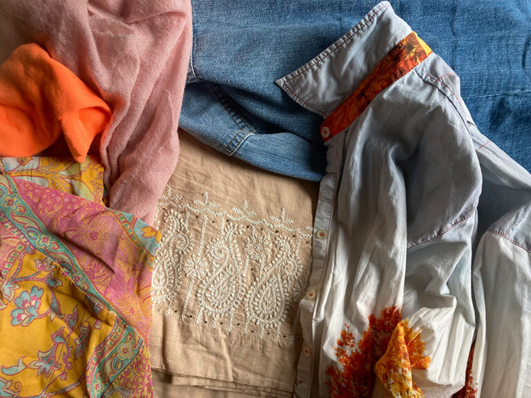 Auf dem Foto liegt bunte Kleidung. Dort ist zum Beispiel ein Schal aus Schafwolle. Und ein Rock aus Kunststoff-Fasern. Und es gibt eine Jacke und eine Bluse aus Baumwolle.