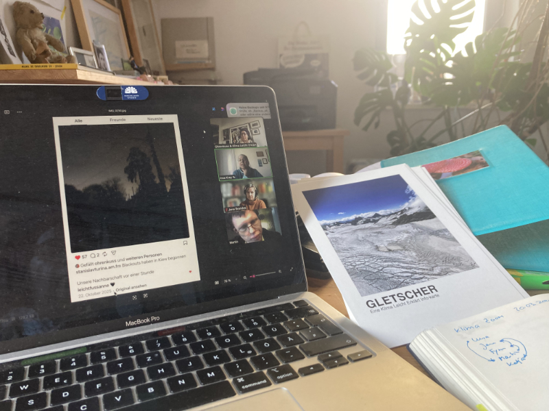 Auf dem Foto ist ein aufgeklappten Laptop zu sehen. Es wird gezoomt. Rechts daneben liegen bedruckte große Karten.