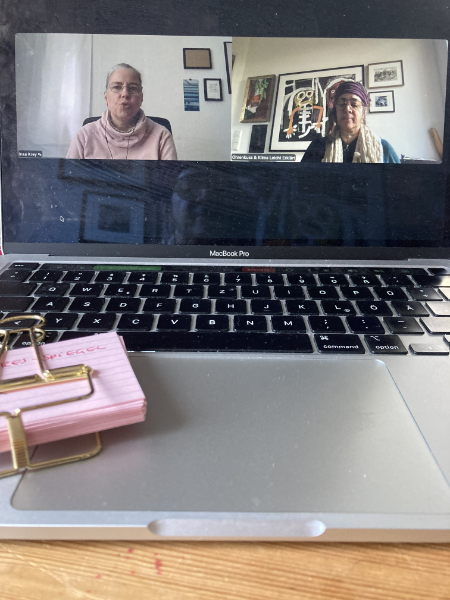 Zwei Frauen sind auf einem aufgeklebten Laptop zu sehen, sie zoomen zusammen. Auf der Tastatur liegt ein Päckchen rosa Karteikarten mit einer Klammer.