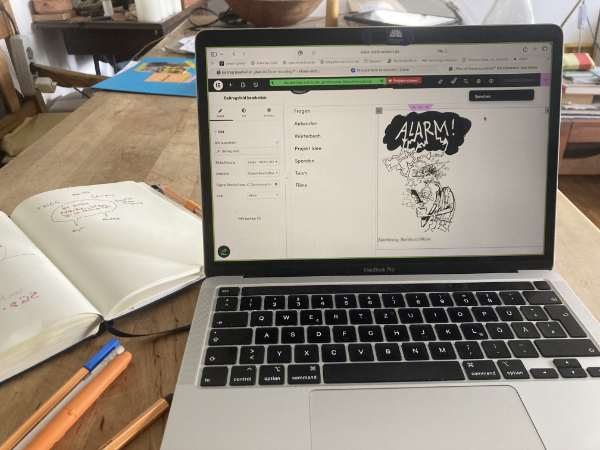 Auf dem Foto sieht man einen geöffneten Laptop. Auf dem Bildschirm ist eine Karikatur zu sehen. Ein Mann hält ein Handy in der Hand und schaut verwirrt. In seiner Gedankenblase ist das Wort ALARM zu lesen.
