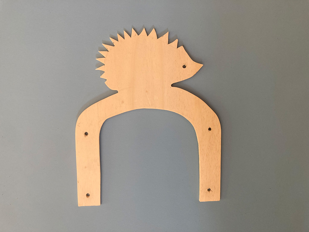 Auf dem Foto ist ein flaches und geschnitztes Stück Holz zu sehen. Es sieht aus wie ein Tor mit einem Igel oben drauf.