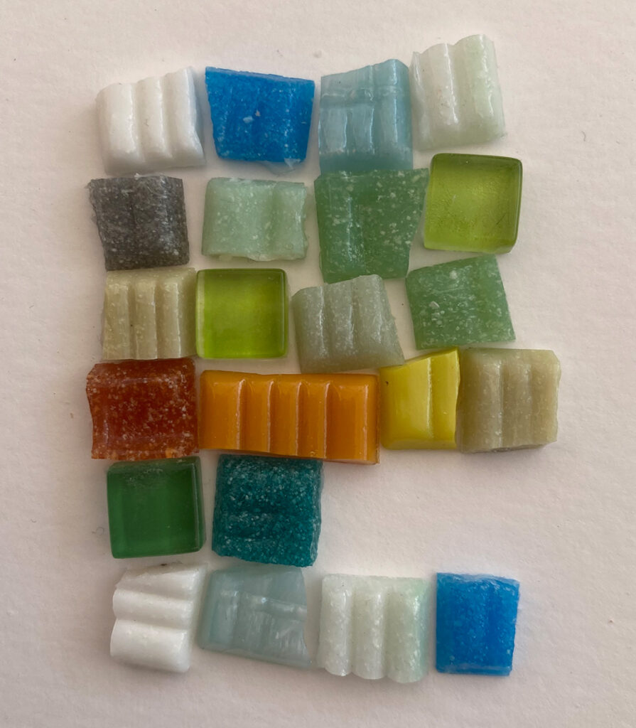 Farbige Mosaiksteine liegen auf einer weißen Fläche.