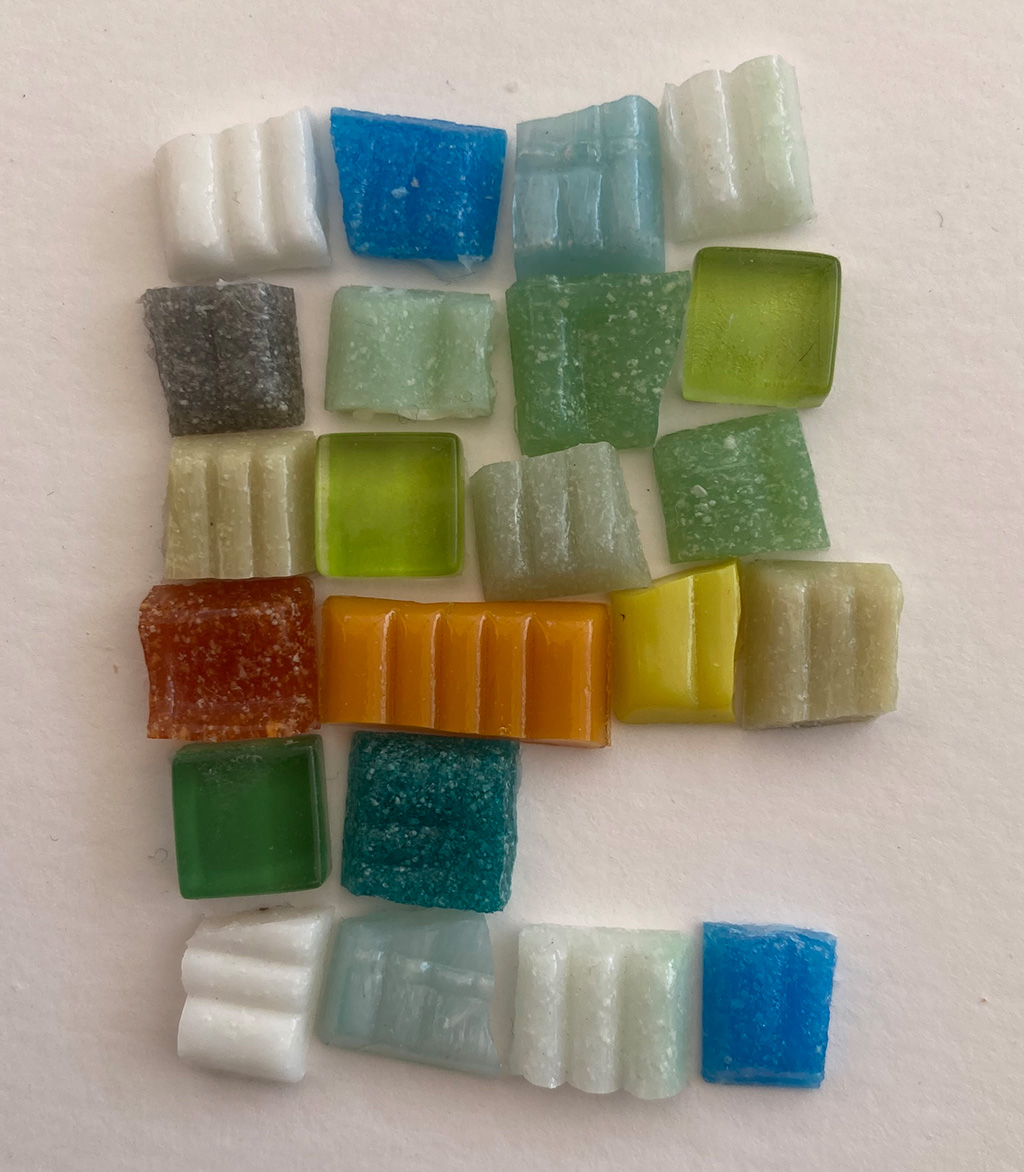 Farbige Mosaiksteine liegen auf einer weißen Fläche.