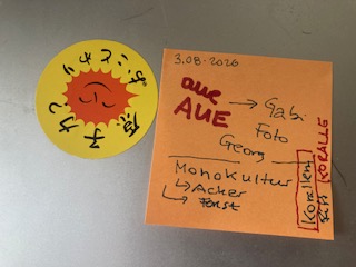 Links ist ein anti Atomkraft Sticker auf Japanisch zu sehen, rechts daneben ein orangener Sticker. Auf dem Sticker stehen einige Worte, unter anderem in roter dicker Schrift AUE