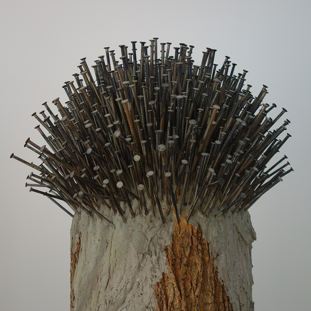 Auf dem Foto sieht man ein Stück Holz. Oben stecken ganz viele Nägel drin. Dadurch sieht das Kunstwerk aus wie ein Igel.
